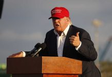 Person speaking at a podium wearing a red hat