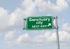 Green road sign saying sanctuary city next exit