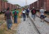 People walking along train tracks carrying backpacks