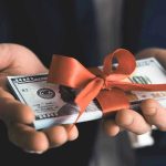 Hands holding stack of hundred-dollar bills with ribbon