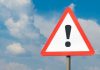 Warning sign with exclamation mark against cloudy sky