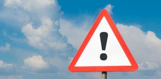 Warning sign with exclamation mark against cloudy sky