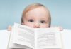 A curious baby peeking over an open book