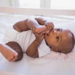 A playful baby lying in a crib, holding their feet