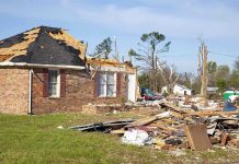 A severely damaged house with debris scattered around from a storm