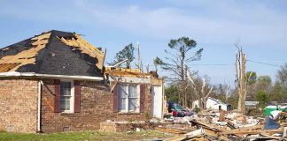 A severely damaged house with debris scattered around from a storm