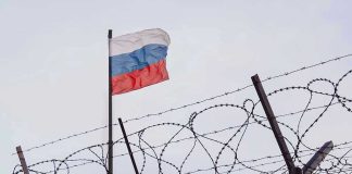 Barbed wire fence with Russian flag in background