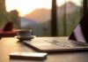 Laptop, coffee cup, and phone on wooden table.