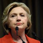 Woman in red jacket speaks into two microphones.
