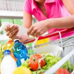 Person holding a shopping list while looking at groceries in a cart