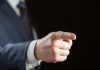 Person pointing with finger, wearing a suit.