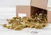 Box of brass bullets spilled on wooden surface.
