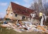 A severely damaged house tilted on its side surrounded by debris