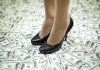 A pair of black high heels standing on a floor covered with dollar bills