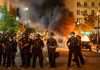 Inferno Rescue Shocks Major City Police officers in riot gear near burning car.