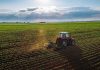 Trump’s China Deal Gives FARMERS HUGE WIN! Tractor plowing a vast green field at sunset.