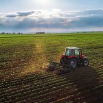 Trump’s China Deal Gives FARMERS HUGE WIN! Tractor plowing a vast green field at sunset.
