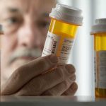 An elderly man holding a prescription bottle while examining it closely