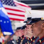 Marines in uniform standing in formation with flags in the background