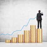 Businessman standing on stacks of coins, drawing a growth chart