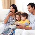 Netflix CAUGHT Pushing Agenda Through Kids Shows A family of four enjoying a movie night on the couch with snacks