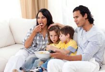 Netflix CAUGHT Pushing Agenda Through Kids Shows A family of four enjoying a movie night on the couch with snacks