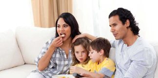 Netflix CAUGHT Pushing Agenda Through Kids Shows A family of four enjoying a movie night on the couch with snacks