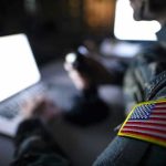 Pentagon’s Secret Weapon Activated! Soldier using laptop with US flag patch visible.