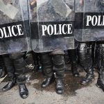 Police officers in riot gear holding shields.