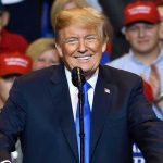 Trump Ignores Racist Smear Storm Man in suit speaking at rally with red hats.