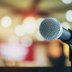 Lip-Sync SCANDAL Backfires — Kid Rock Fires Back Microphone with blurred lights in the background.