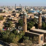 Axe-Wielding Men Storm Mosque Aerial view of a city featuring traditional buildings and minarets