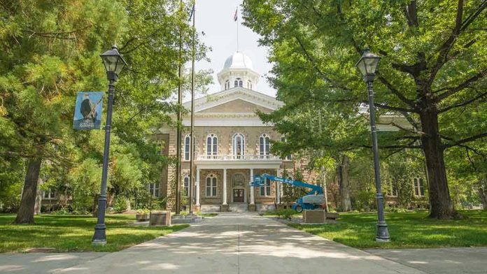 1830490232 Historic stone building surrounded by trees and lampposts.