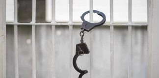 Handcuffs hanging on white metal bars.