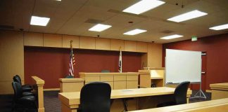Firefighter’s Shocking Gun Attack—What Drove Him? Interior view of an empty courtroom with wooden furniture and American flags