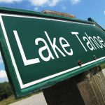 A green directional sign pointing to Lake Tahoe against a blue sky