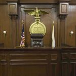 Insurance Cash, Dead Family — What Broke Him? Judges bench in an empty courtroom, scales emblem above.