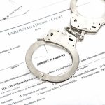 Federal Arrest Puts Minnesota Fraud Back In Spotlight Handcuffs on top of an arrest warrant document.