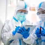 Ebola Outpaces Response—No Vaccine Ready Two healthcare workers in full PPE reviewing a clipboard
