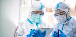 Two healthcare workers in full PPE reviewing a clipboard