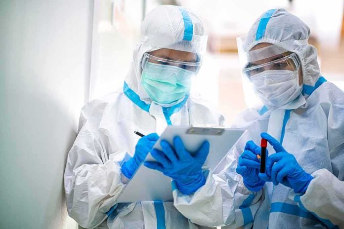 shutterstock_1695624856 Two healthcare workers in full PPE reviewing a clipboard