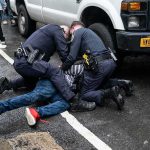 NYPD Cop Faces 7 Years After Illegal Chokehold Conviction Police officers restraining a person on a wet city street beside a truck