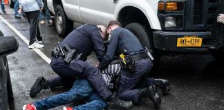NYPD Cop Faces 7 Years After Illegal Chokehold Conviction Police officers restraining a person on a wet city street beside a truck