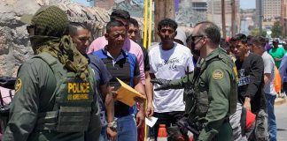 Border patrol officers speak with a line of people outdoors