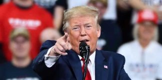 Trump Teases MASSIVE Iran Strike Man in suit pointing, speaking at a rally.