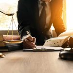 County Gives $2,000 to Illegal Alien Families After ICE Detentions Lawyer writing at desk with scales and gavel