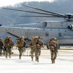 Soldiers disembark and walk past a large military helicopter