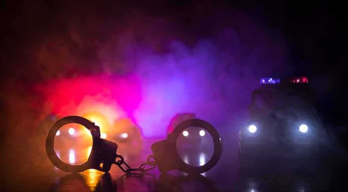 shutterstock_1137130418 Handcuffs on a surface with police cars and flashing lights in smoky darkness