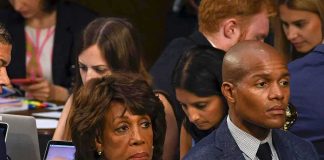 Maxine Waters seated among attendees at an indoor event