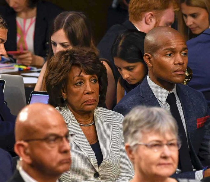 shutterstock_1227480913 Maxine Waters seated among attendees at an indoor event